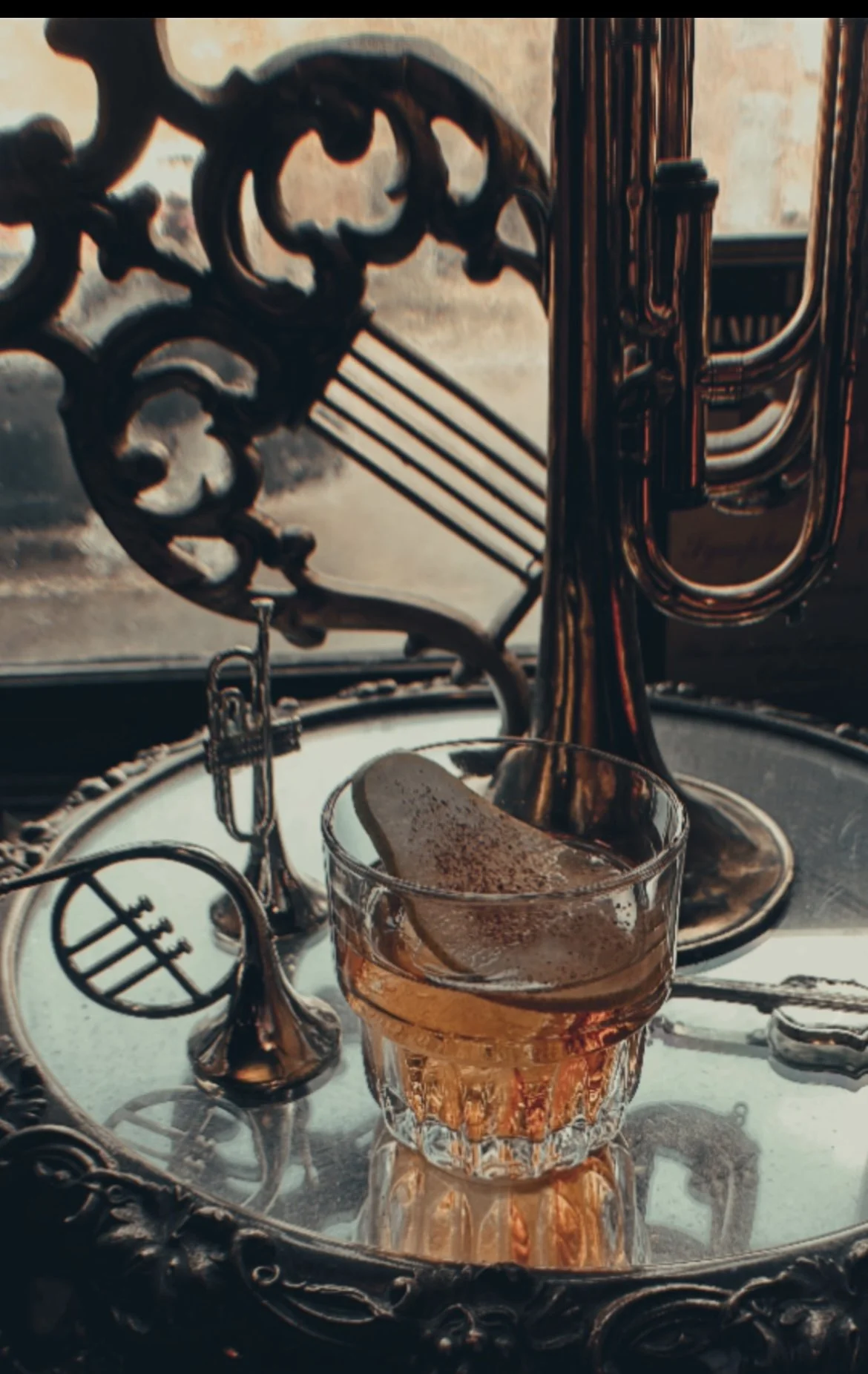 An old fashioned garnished with dehydrated pear, served beside a brass trumpet